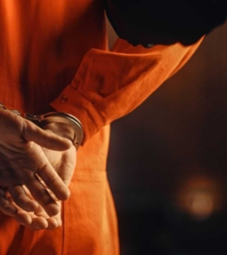 Close-up of a person in orange prison attire with handcuffed hands