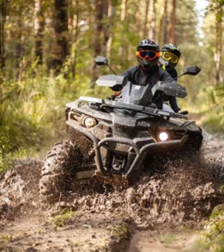 Rider on an all-terrain vehicle (ATV) navigating through a muddy trail in the forest