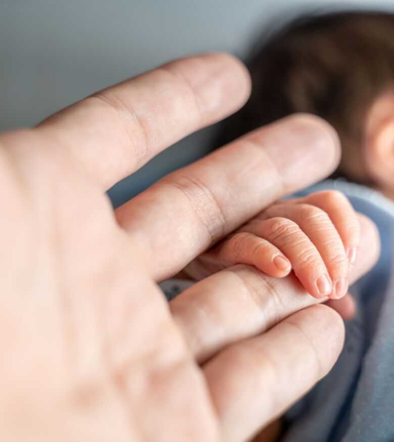 Close-up view of a newborn baby's hand gripping an adult's finger