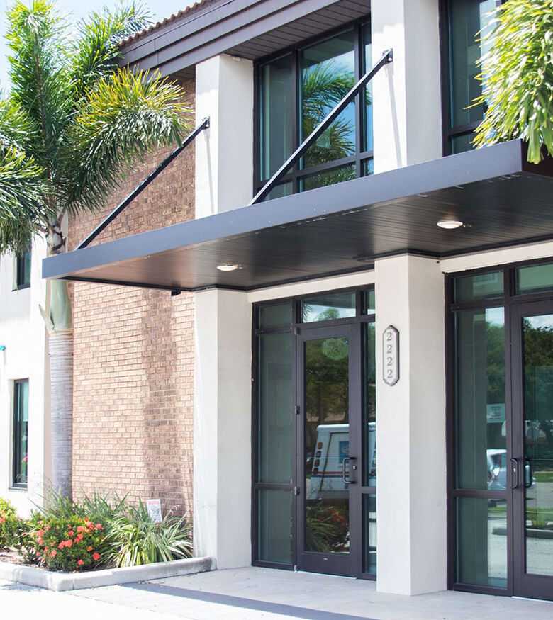 Modern office building facade in Sarasota with glass doors and surrounded by palm trees, suitable for Personal Injury Lawyers.
