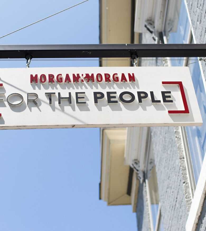Street sign reading 'Morgan & Morgan FOR THE PEOPLE' advertising Personal Injury Lawyers in New Albany against a blue sky.