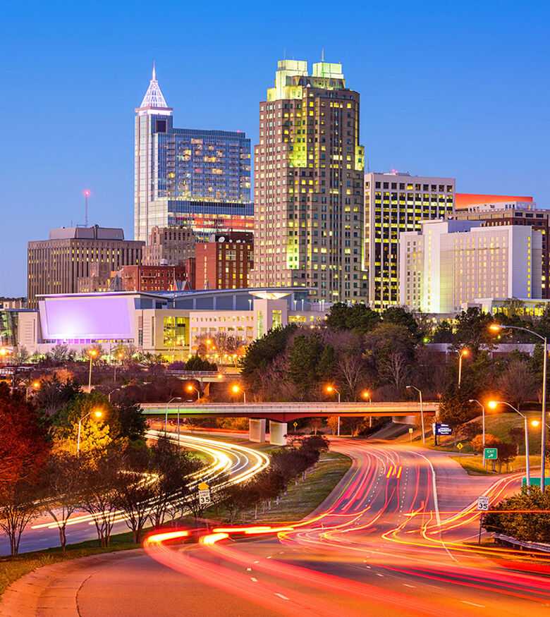 Twilight view of Raleigh skyline with lit buildings and busy highways, an urban hub for Personal Injury Lawyers.